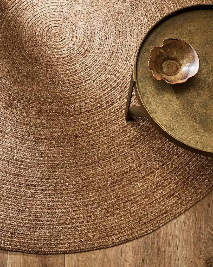 A table, indoors, sitting on top of a round brown indoor/outdoor rug by Baya NZ