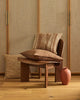 A textural, woven cushion in warm brown tones, on a chair with a complementary design