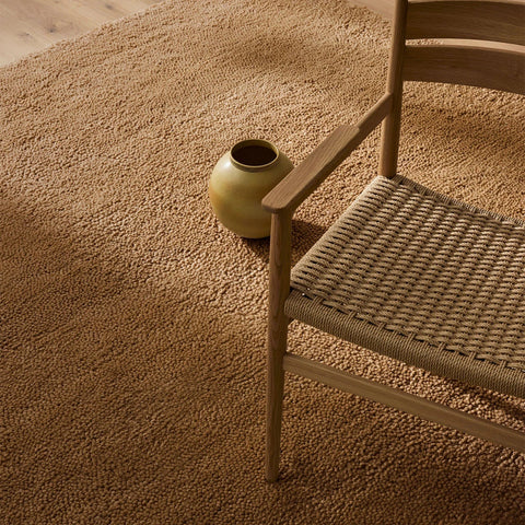 A beautiful caramel-brown wool rug, with thick and plush cut pile - the Valencia Camel, seen in a room under a  stylish chair.