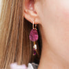 Close up of burgundy earrings with gold findings and a freshwater pearl charm, worn by a model