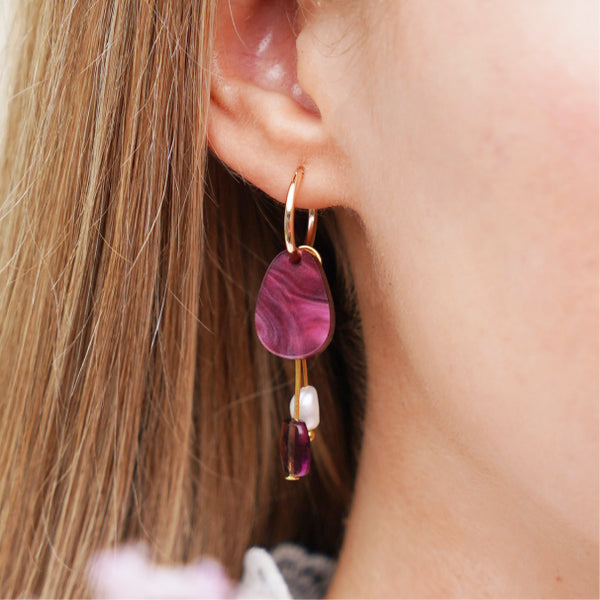 Close up of burgundy earrings with gold findings and a freshwater pearl charm, worn by a model