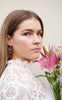 Merlot-coloured dangle earrings with pearl charm, worn by a model in a white dress