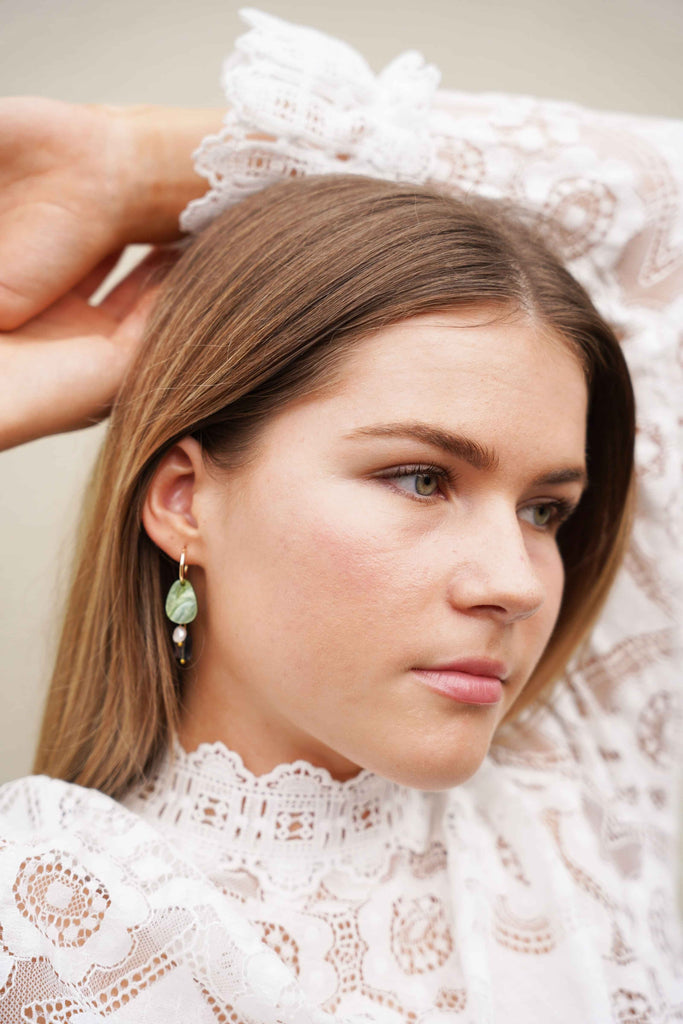 A model wearing NZ designer Hagen + Co's earrings featuring green acrylic, blue glass and a freshwater pearl charm