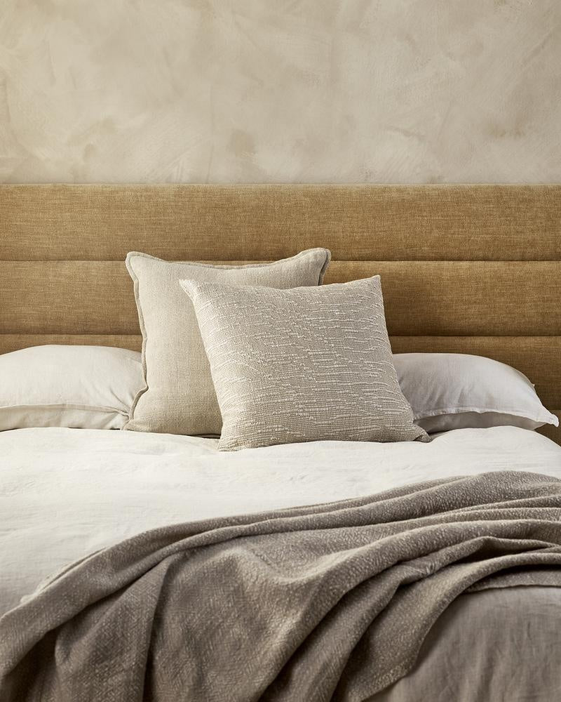 Beige designer cushions by Baya NZ, seen on a bed in a modern bedroom.