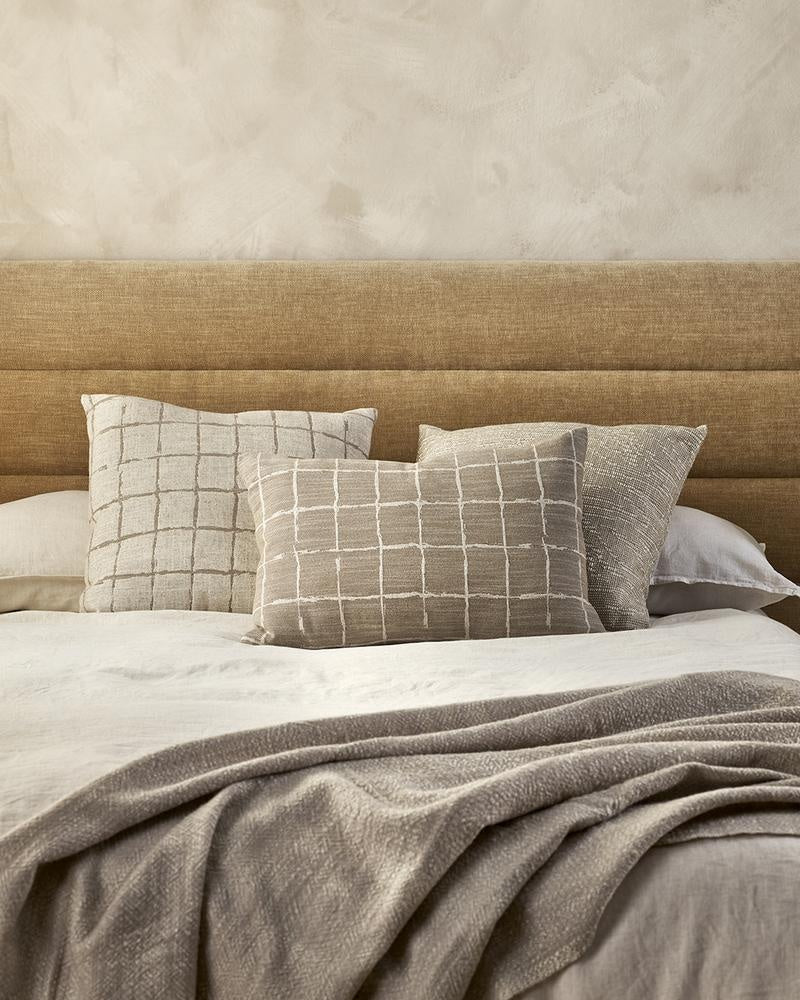 Three beautiful cream and beige designer cushions by Baya, on a bed in a stylish modern bedroom.