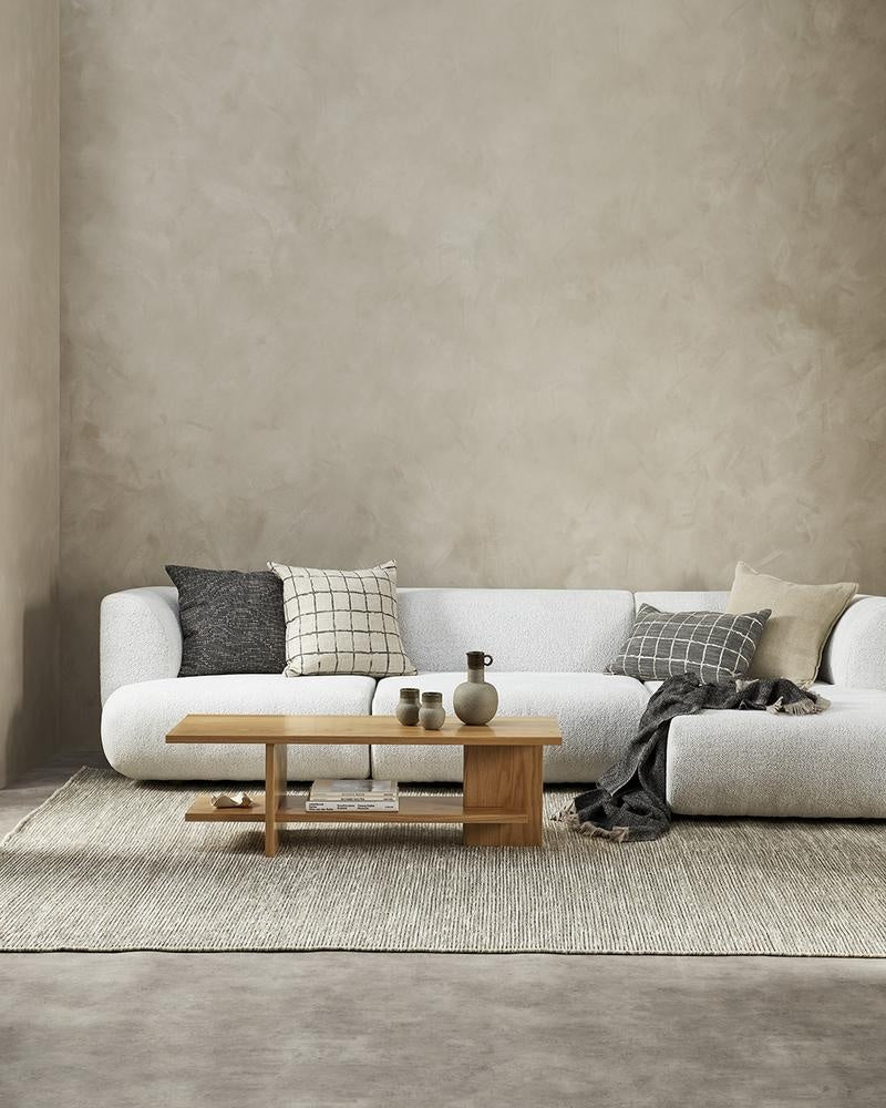 Designer cushions inn brown tones, on a white couch in a modern living room with coffee table.