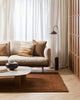 A stylish living room decorated in warm brown and cream tones, with a feature pillow in shades of cream and tan, patterned with sand dunes. By Baya. 