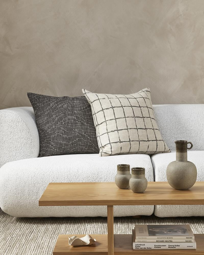 The modern patterned Harrison cushion by Baya, featuring a grey/black grid design in a hand-painted style on a natural linen-look base, close up next to a black pairing cushion on a creamy-white couch.