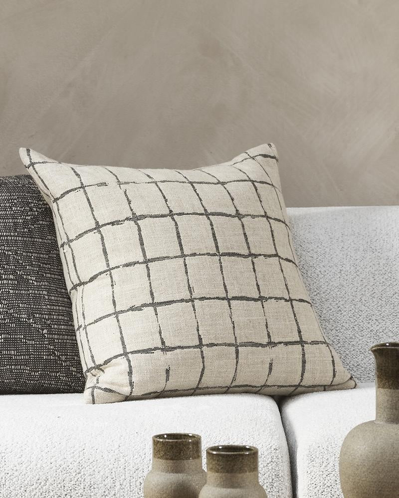 The Baya Harrison cushion in black, featuring a  grid-like design with a handcrafted look on a linen blend base, next to a black textural cushion.