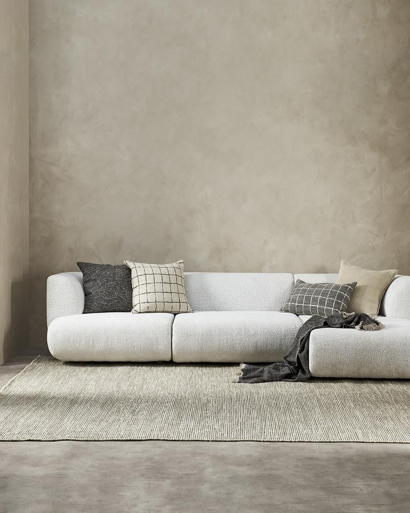 A minimalist living room featuring a white couch and complementary designer cushions in black and natural linen colours, by Baya.