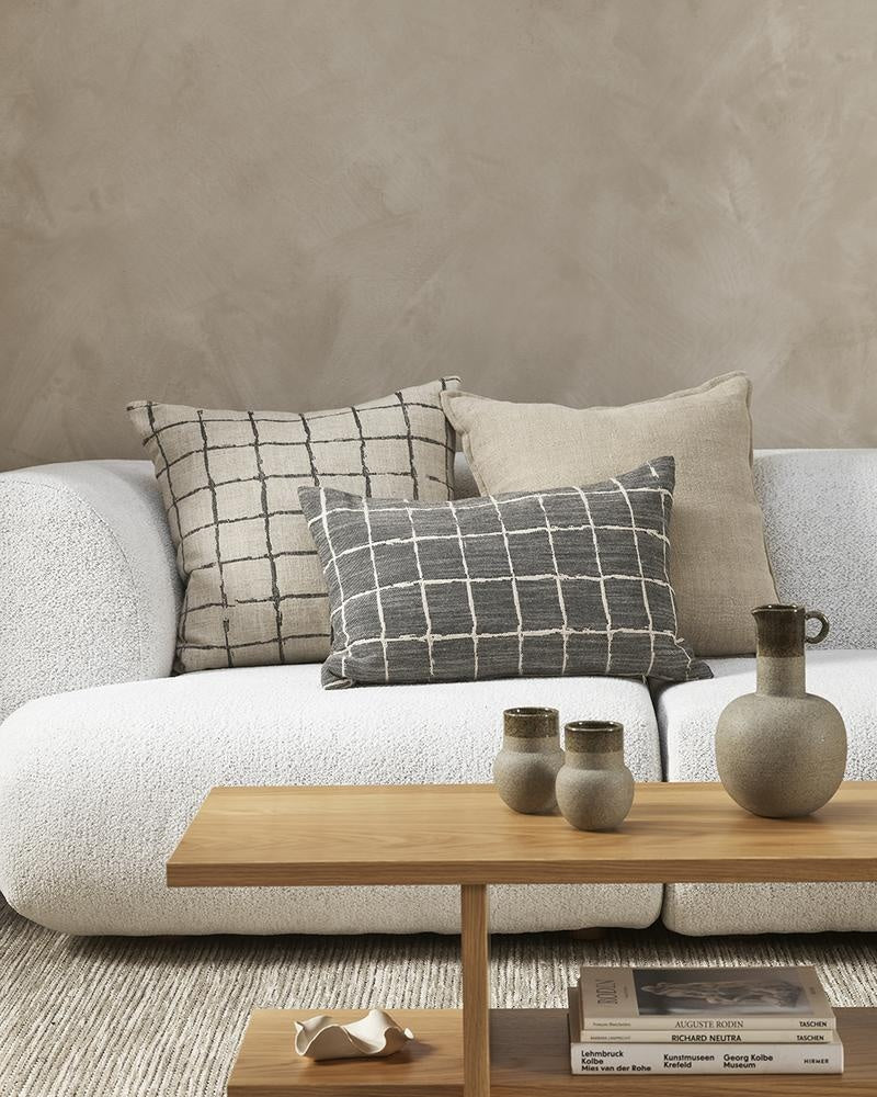 Complementary designer cushions in natural linen colours and black, styled on a white couch in a modern NZ living room.