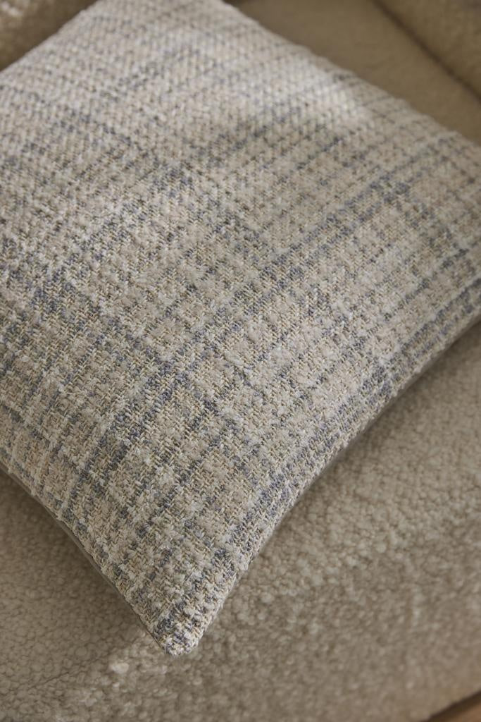 An on-trend woven cushion in white, alongside subtle beige and blue - the Tripoli Pearl by Weave, on a cream boucle couch