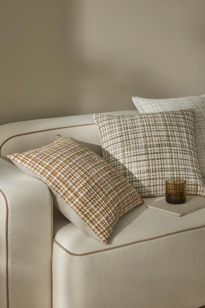 Designer cushions in a textural weave featuring warm brown, oranges, taupe and creamy whites, sitting on a couch in a serene room