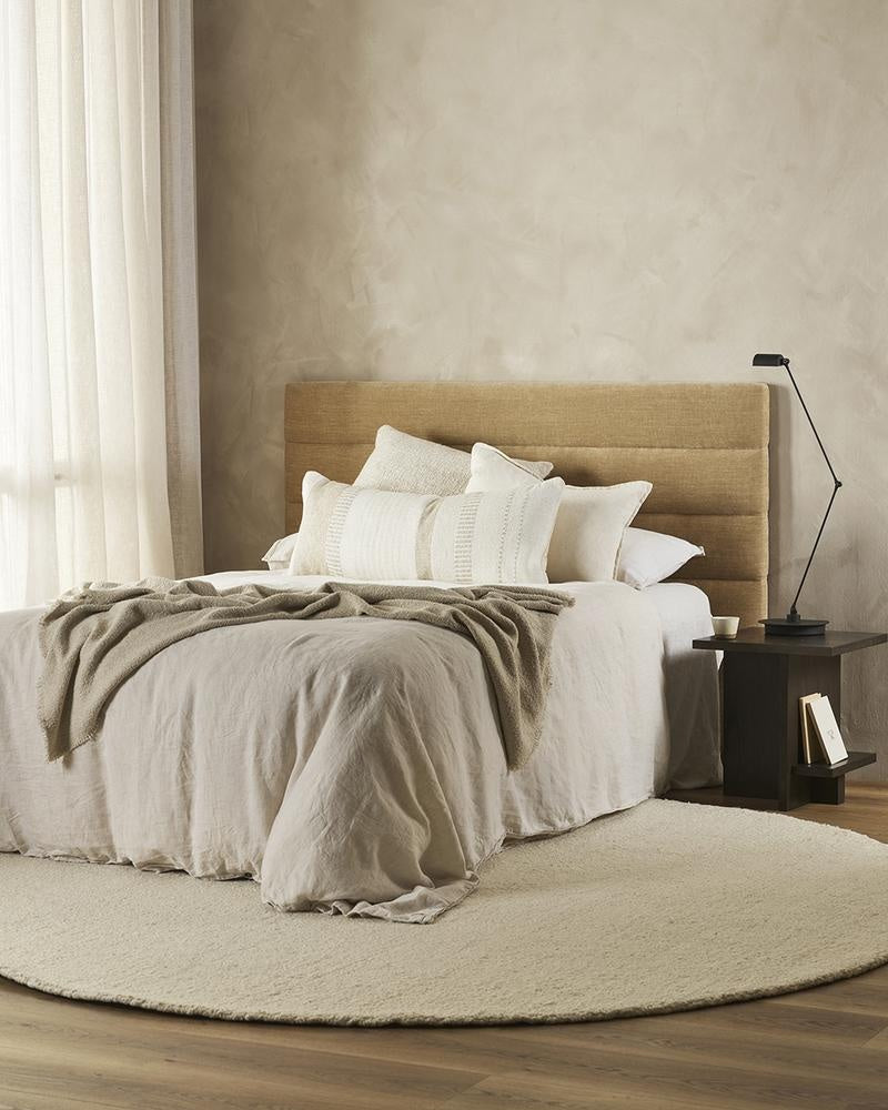 An extra-long lumbar cushion in white and beige - the Bettie by Baya -seen on a bed in a stylish bedroom.