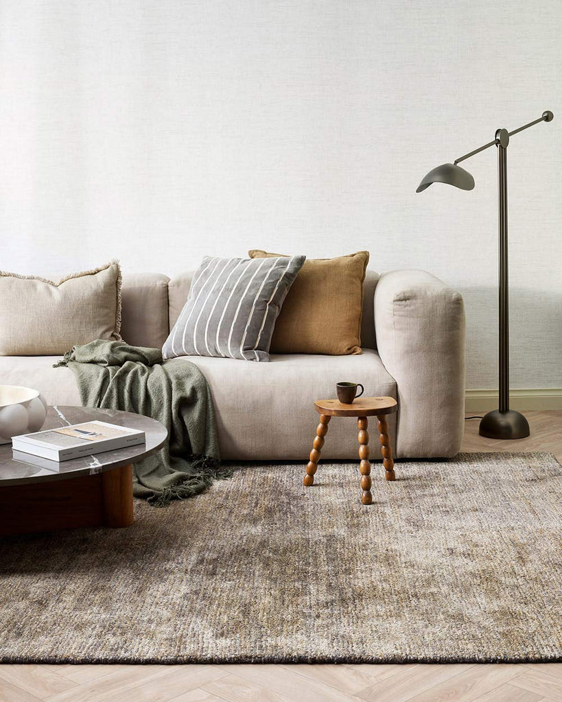 A living room with a textured handmade floor rug in shades of warm grey and honey brown, made with natural jute fibres  and bamboo silk by Baya. 