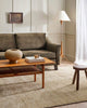 A stylish living room in earthy green and neutrals, with a textured handwoven floor rug in shades of warm beige and natural jute brown. By Baya