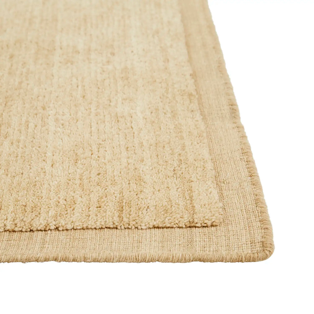The corner of a 100% wool rug in a soft caramel colour with a contrast frame detail, the Bower Frame Butter  by Soren Liv