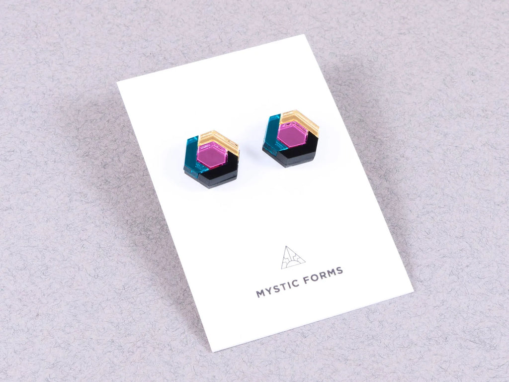 Hexagonal acrylic earrings in pink, teal and gold, by Mystic Forms, on a card