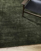 The deep green Haywood 'Caper' floor rug, tip-sheared in NZ wool, seen on wooden floorboards under a chair in a modern home.