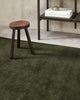 The deep green Haywood 'Caper' floor rug, tip-sheared in NZ wool, seen in a contemporary space under a stool.