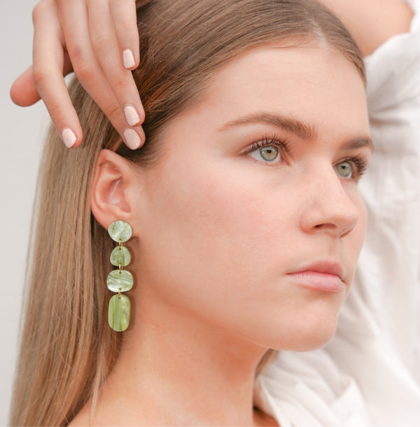 Close up of a model wearing Hagen + Co's green marbled-acrylic dangle earrings