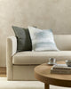 The Baya Flaxmill pure linen cushion in Sage Green next to the Baya Sunset cushion, on a couch in a modern living room