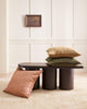 Three textured linen cushions in tones of warm sandy beige, deep green and muted clay pink, atop a coffee table, by Baya. 