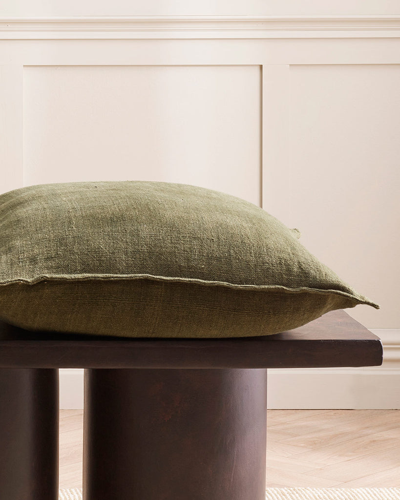 A table with a cushion on it in a deep winter green with a textured linen weave. By Baya