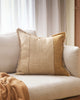 A soft brown cushion with stripe detailing and a fringed edge, on a cream toned couch