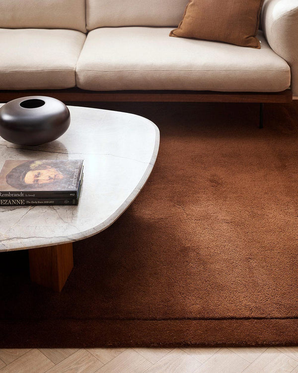 A close up of a stylish cream and brown toned living room with a luxurious chocolate coloured cut pile floor rug in 100% NZ wool. 