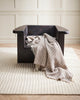A 100% wool throw blanket draped over a chair, in neutral beige colours, with cream twisted edging.