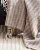 A detailed view of a striped throw blanket with soft cream twist edging, in 100% wool. 