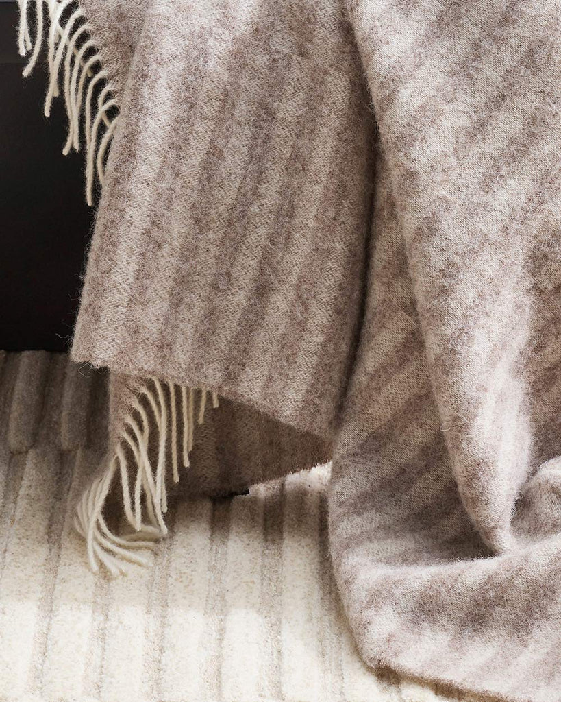 A detailed view of a striped throw blanket with soft cream twist edging, in 100% wool. 