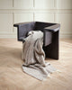 A neutral striped throw blanket in 100% wool with cream twisted edging, over a designer chair. 