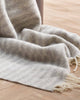 A detailed view of the striped Noah blanket in neutral silver with cream twisted edgings, in 100% wool. 