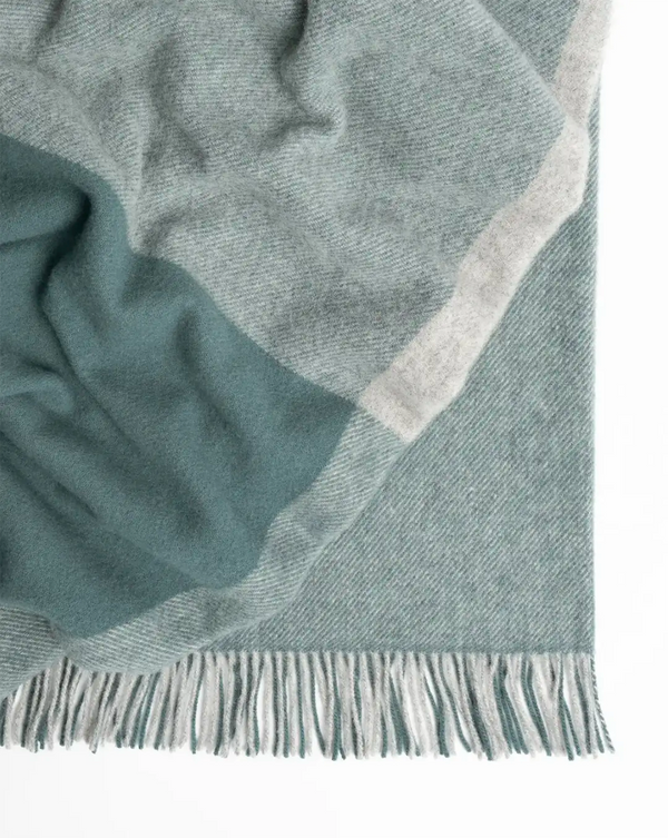 A light, warm blue with mid-grey contrast wool throw blanket with fringe