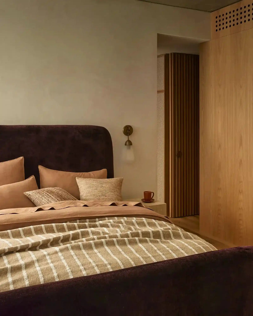 Brown and white striped throw blanket at the end of a bed in a stylish bedroom