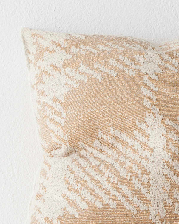 A close up image of a textural check patterned cushion in shades of light orange and off-white. 