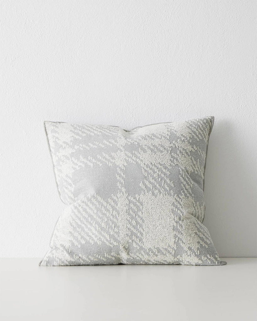 A textured cushion with an oversized check pattern in tones of grey, off white and light blue. 