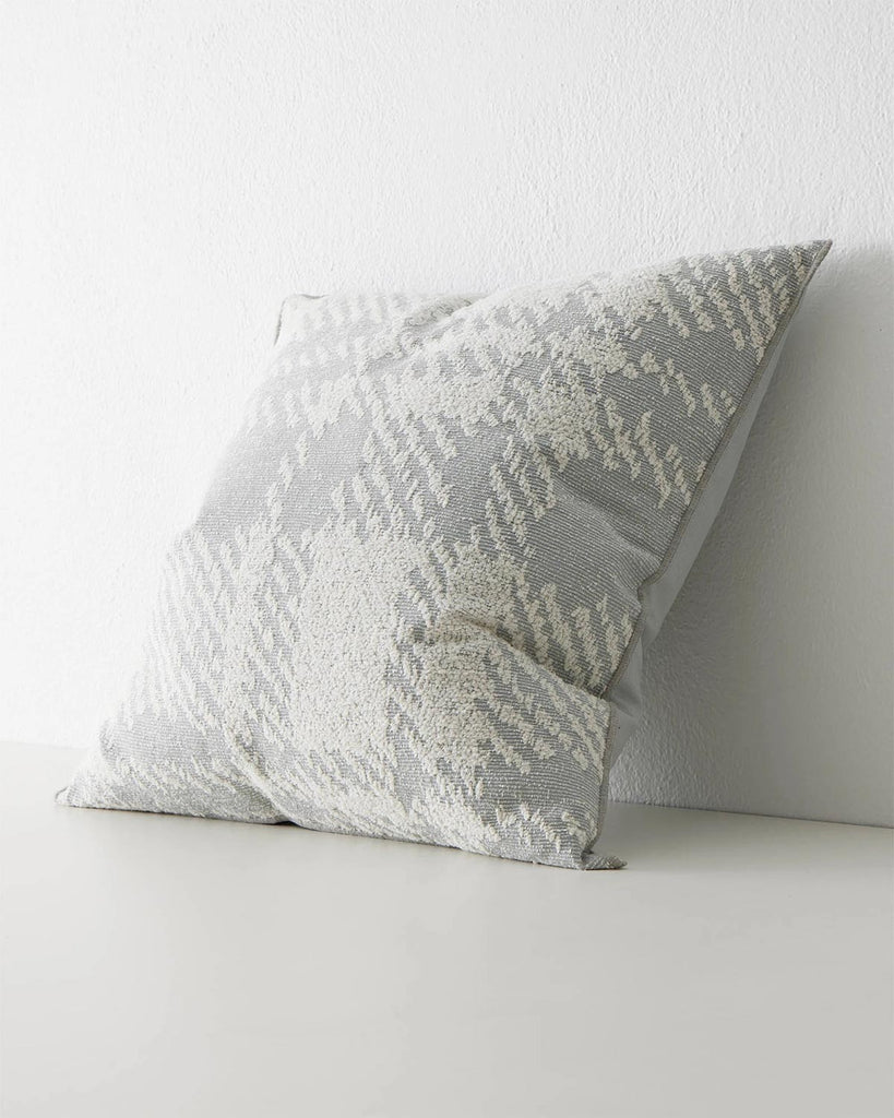 A side long image of a square cushion with a textured check pattern in shades of muted light blue and white. 