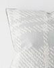 A close up view of a cushion with a textured check pattern in blue-grey and white. 