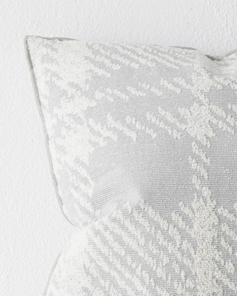 A close up view of a cushion with a textured check pattern in blue-grey and white. 