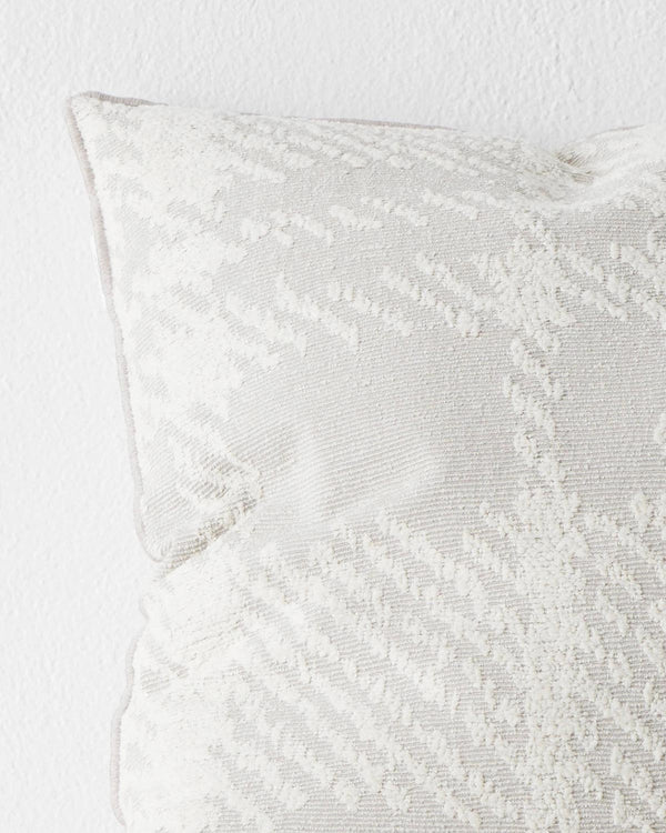 A close up view of a textural check patterned cushion in shades of white and light grey. 