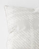 A close up view of a textural check patterned cushion in shades of white and light grey. 