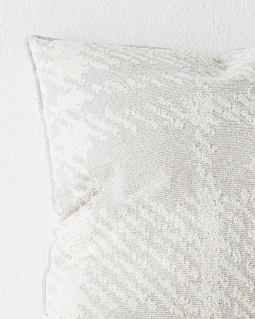 A close up view of a textural check patterned cushion in shades of white and light grey. 