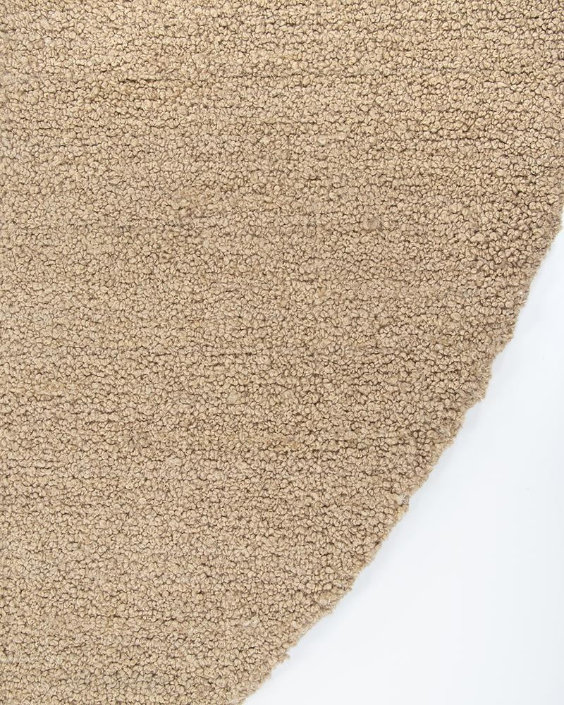 Th curved edge of the light-brown 'Biscuit' boucle floor rug by Baya nz, showing the boucle effect of the weave