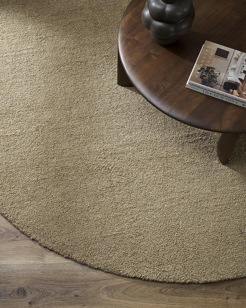 A sophisticated round wool floor rug in a boucle weave in light-mid brown colour - the Dorset Biscuit by Baya, seen in situ undera coffee table.