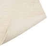 Corner of a creamy white wool-blend floor rug featuring an abstract horizontal pattern, folded to show underneath