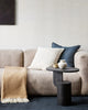 A soft beige modern couch with two cushions, one in blue linen and one cream with navy vertical stripes, by Baya. 