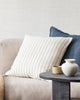 Two cushions in complimentary tones of blue and cream, one a solid blue linen, one with a handwoven pattern of linear navy stripes on an off white background, on a modern style couch. By Baya